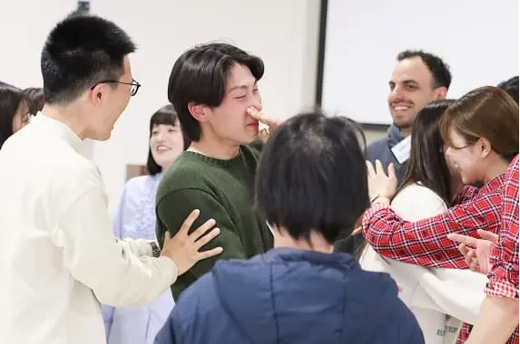 最終発表を終えて感極まる参加者を仲間たちが囲んで称え合う様子