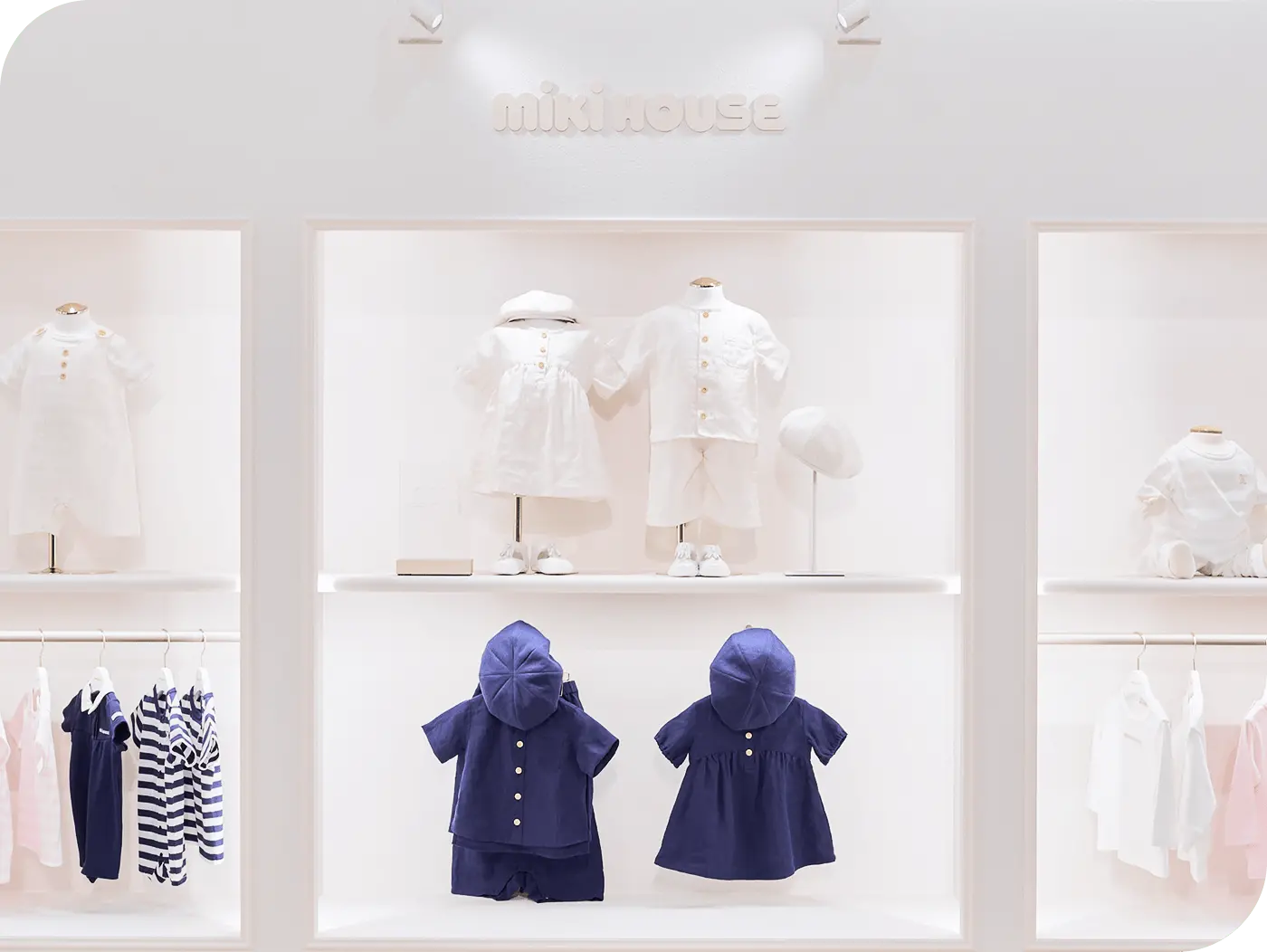 白を基調とした明るいミキハウスの店舗内観。中央のディスプレイには紺色のベビー服が並び、周囲の棚には白やピンクの子ども服が展示されている様子
