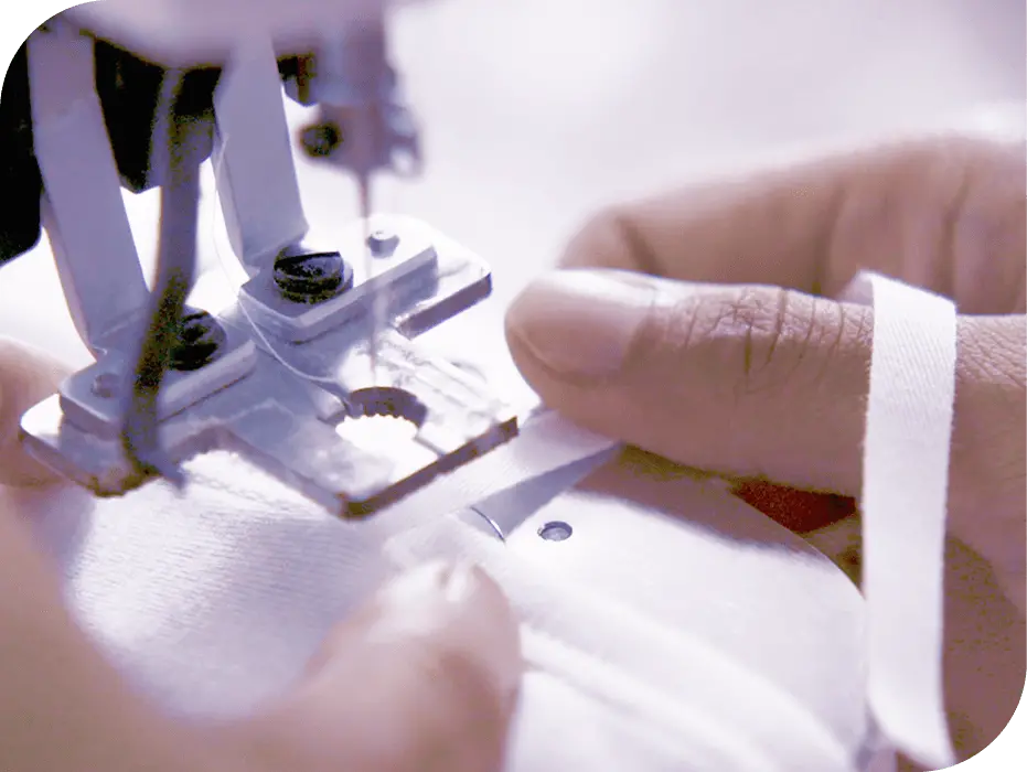 ミシンで白い生地を縫製する様子。指先で生地を丁寧に押さえながら作業している職人の手元